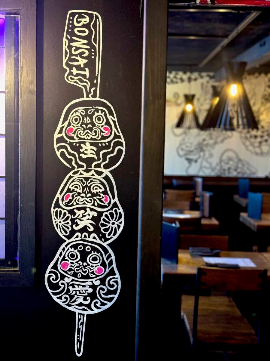 Image of "Daruma Skewers", a mural by Megu Ueda. The three Darumas are stacked on top of eachother and skewered like a dango or yakitori.