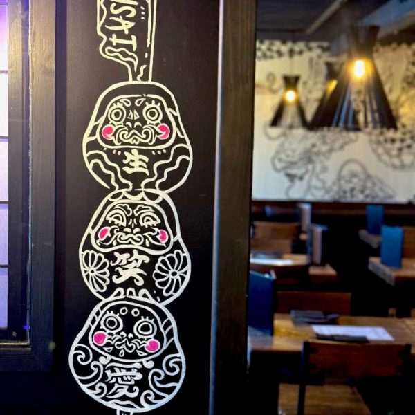 Image of "Daruma Skewers", a mural by Megu Ueda. The three Darumas are stacked on top of eachother and skewered like a dango or yakitori.
